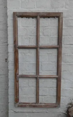 A wooden window frame with six panes is mounted on a white brick wall.