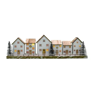 A row of five illuminated wooden houses with Christmas trees in front of them, set against a white background.