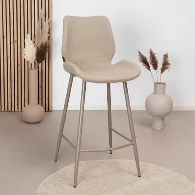 A beige bar stool is placed on a rug in a room with decorative vases and dried plants.