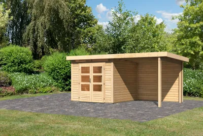 A wooden garden shed with an attached canopy, set on a paved area in a garden with trees and bushes.