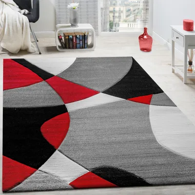 A modern geometric rug in red, black, and gray is displayed in a well-lit living room setting.