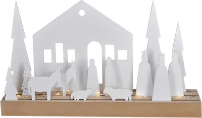 A white nativity scene with figures of people, animals, and trees on a wooden base, illuminated by small lights.