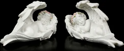 Two white angel figurines with pink floral accents, lying down with wings spread, against a black background.