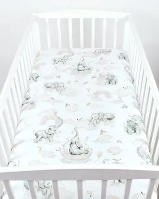 A baby crib with a fitted sheet featuring a pattern of elephants and clouds.