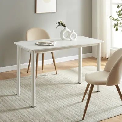 A white dining table with two chairs in a room with a grey wall and a window.