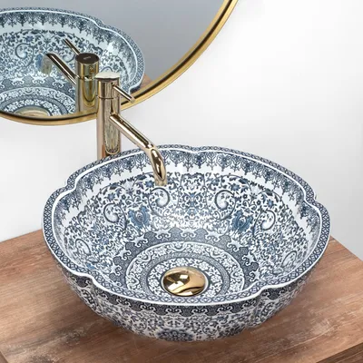 A close-up view of a decorative blue and white patterned vessel sink with a gold faucet.