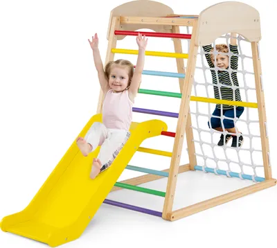Two children playing on a wooden indoor climbing frame with a slide and climbing net.