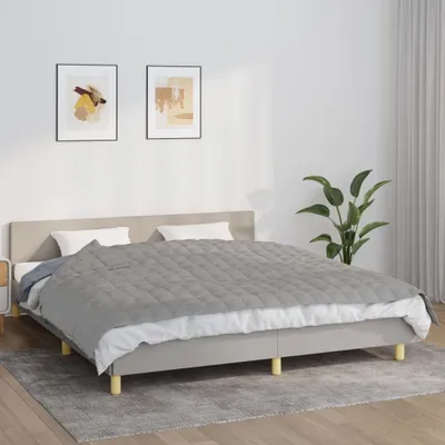 A bed with a gray blanket and white pillows in a room with two framed pictures on the wall and a plant.