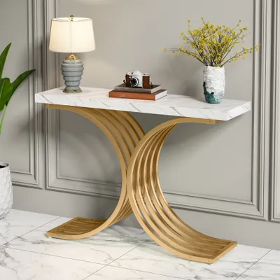 A console table with a marble top and gold metal legs, decorated with a lamp, books, a camera, and a vase of flowers.