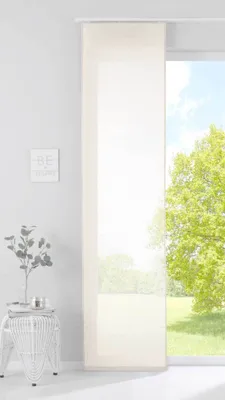 A panel curtain hangs in front of a large window with a view of a green tree and blue sky. A small white side table with a plant is to the left.
