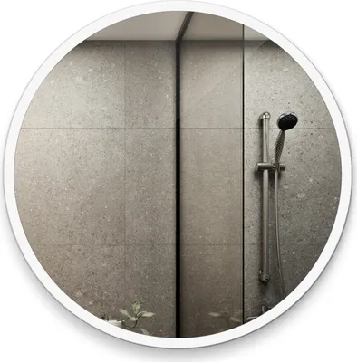 A round mirror with a white frame reflecting a tiled shower wall and a shower head.