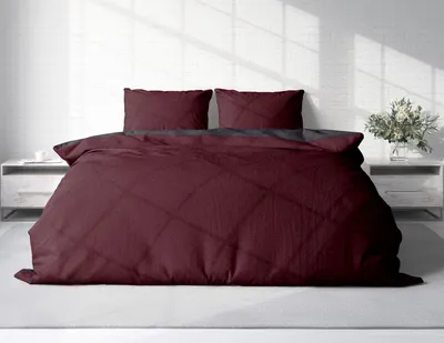 A bed with burgundy and anthracite bedding in a room with white brick walls.