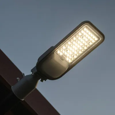 A close-up of an LED street light mounted on a dark structure against a clear sky.