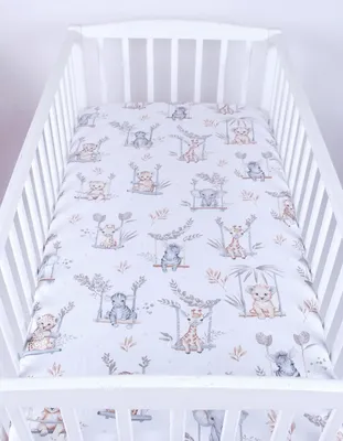 A crib with a fitted sheet featuring a pattern of cartoon animals.