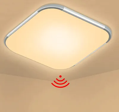 A square-shaped LED ceiling light with a silver frame and a frosted white diffuser, mounted on a beige ceiling. A red graphic indicating motion detection is shown below the light.