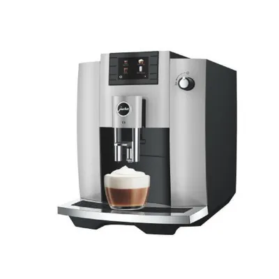 A JURA E6 coffee machine is shown against a white background, with a cup of coffee with foam in the foreground.