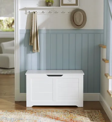 A white storage bench is placed in a hallway with a coat rack and a hat hanging above it.