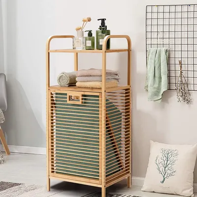 A bamboo shelf unit with a laundry basket and folded towels, placed in a room with a wall grid and a decorative pillow.