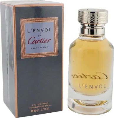 L'Envol de Cartier Eau de Parfum, goldener Duft im runden Glasflakon mit silberner Kappe, daneben anthrazitfarbene Box mit Kupferrahmen.