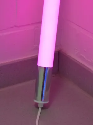A close-up of the base of a pink LED light stick standing on a tiled floor next to a wall.