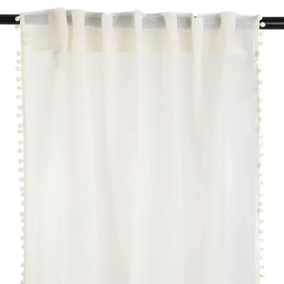 A close-up view of a cream-colored curtain with pom-pom trim hanging from a curtain rod.