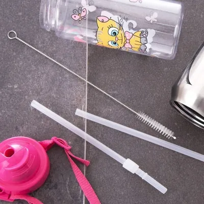 A close-up view of cleaning brushes and straws for a baby bottle, with a pink lid in the foreground.