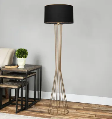 A floor lamp with a black shade and a gold metal base stands next to a set of nesting tables with a plant and a book on them.