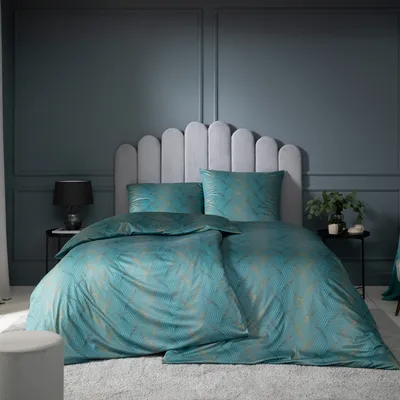 A bedroom scene with a bed dressed in teal bedding with a gold pattern, against a dark gray paneled wall.