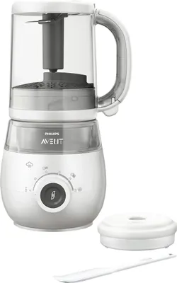 A white baby food maker with a transparent jug and a gray interior is shown against a white background. Accessories are placed to the right of the main unit.