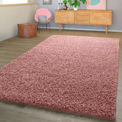 A pink shaggy rug is laid out on a wooden floor in a room with a wooden cabinet and a chair.