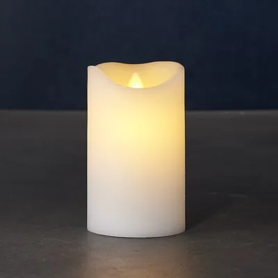 A white LED candle with a flickering yellow flame sits on a dark gray surface against a dark blue background.