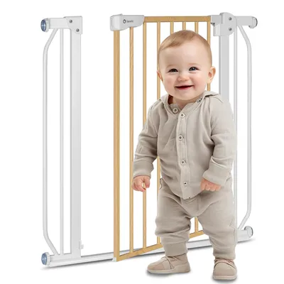A baby stands in front of a baby gate.