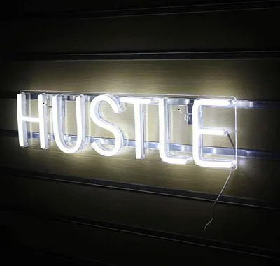 A white neon sign spelling out "HUSTLE" mounted on a slatted wall.