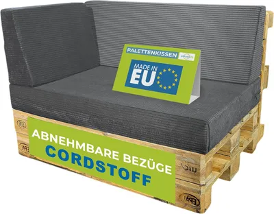 A dark gray cushion set for a pallet sofa, displayed on a wooden pallet base. A green sign with EU stars and text is placed on the cushions.