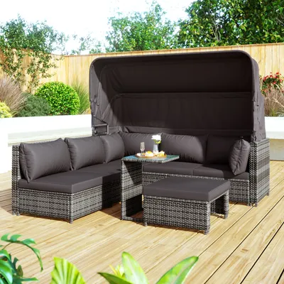 A polyrattan garden lounge set with a canopy and cushions is placed on a wooden deck, surrounded by greenery and a fence.