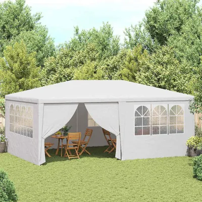 A white party tent set up in a grassy backyard with trees in the background. A table and chairs are visible inside the tent.