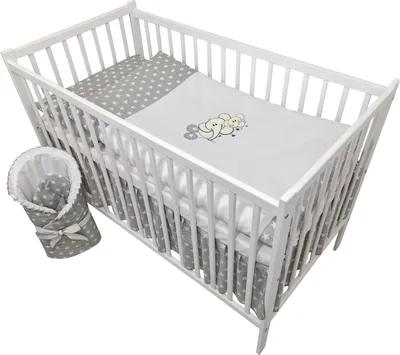 A white wooden crib filled with baby bedding. A grey and white star-patterned blanket is rolled up and tied with a bow to the left of the crib.