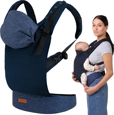 A woman is holding a baby in a dark blue baby carrier. The baby carrier is also shown separately on the left side of the image.