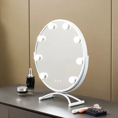A white makeup mirror with lights sits on a gray dresser next to some cosmetic products.