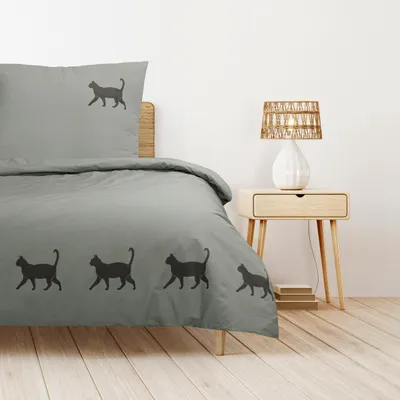 A bed with a duvet cover and pillowcase featuring a cat silhouette pattern, placed in a bedroom setting with a nightstand and lamp.