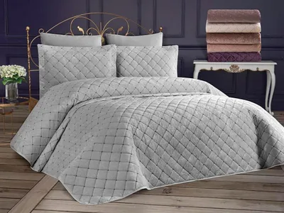 A neatly made bed with grey quilted bedding and pillows, set against a dark purple wall and a decorative white table with stacked towels.