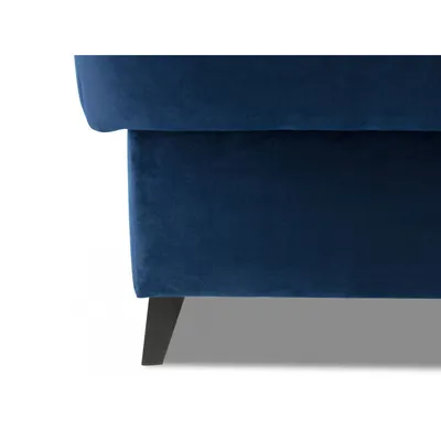 A close-up view of the bottom corner of a blue velvet ottoman with black wooden legs.