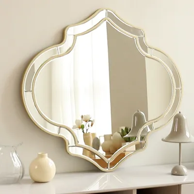 A decorative mirror is displayed on a white surface, reflecting a room with curtains and lamps.