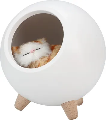 A white, spherical pet house with wooden legs, containing a sleeping plush cat.