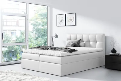 A white upholstered bed with a mattress and bedding in a bright, modern bedroom with large windows.