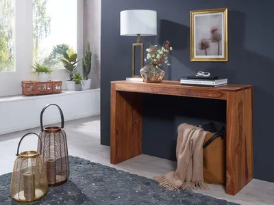 A console table with a lamp, vase, and books on top, placed in a room with a window and decorative lanterns.