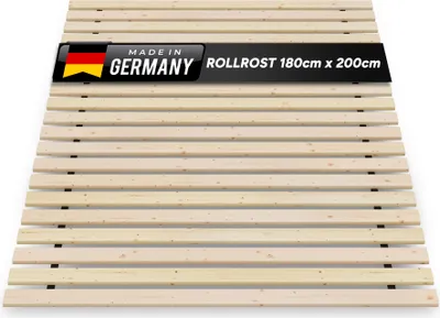 A wooden slatted bed base, also known as a rollrost or lattenrost, is shown from a slightly elevated diagonal angle against a white background. A black banner with text and the German flag is overlaid on the top portion of the bed base.