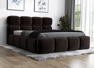 A modern upholstered bed with a tufted headboard and frame, set on a rug in a room with artwork and a window.