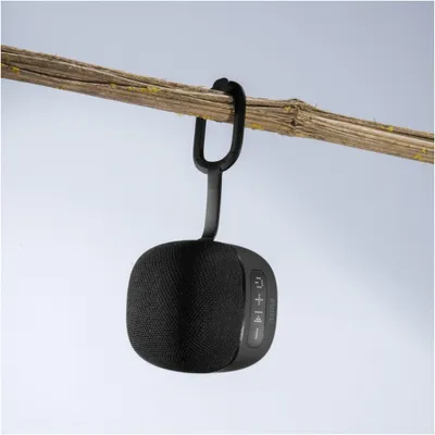 A black Hama Cube 2.0 Bluetooth speaker is hanging from a branch by its strap.