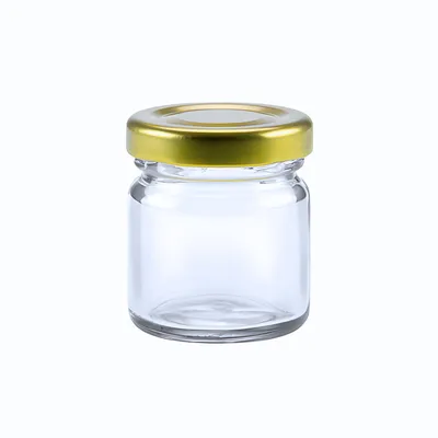 A clear, studio shot of a small, empty glass jar with a gold metal twist-off lid, isolated on a white background.